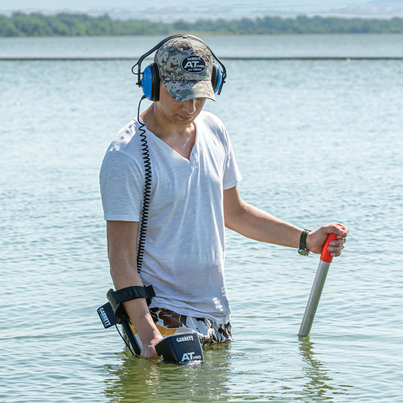 A man standing in a lake metal detecting underwater.
